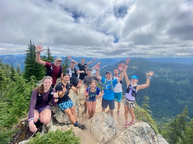 A group of runners celebrating summiting the top of a mountain, their hands raised in the air